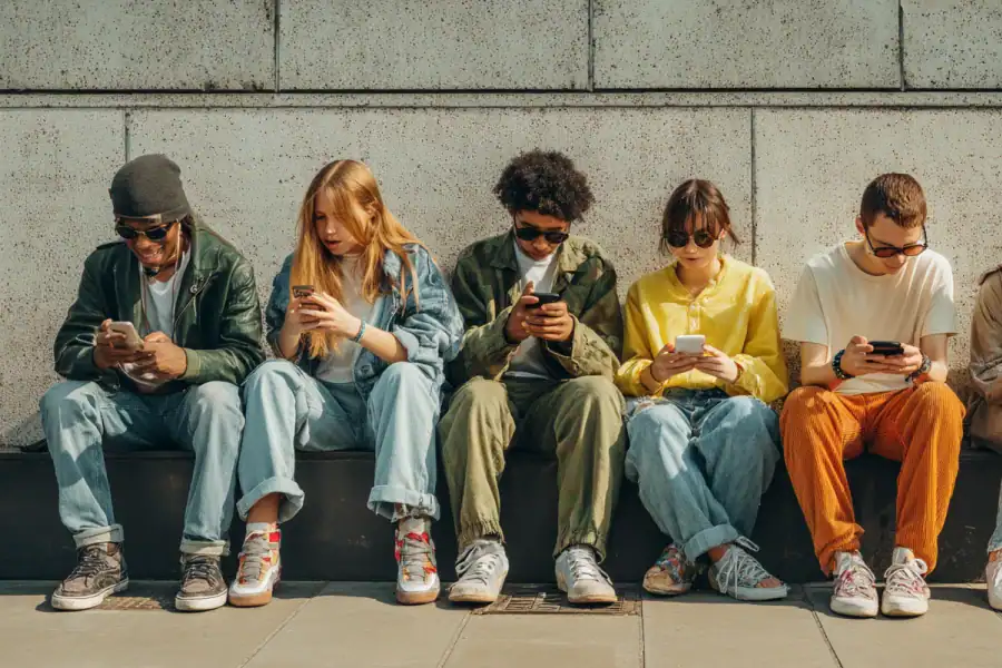 Young diverse people using smartphones while sitting against concrete wall Outdoor scene for social media, technology, and youth culture SEO keywords.