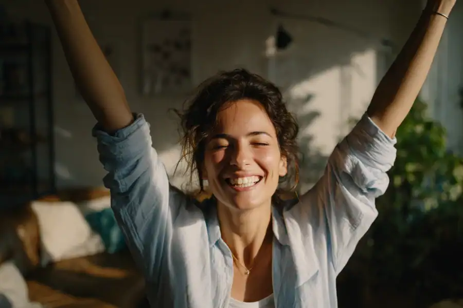 Smiling woman stretching in sunlight, enjoying a cheerful morning at home.