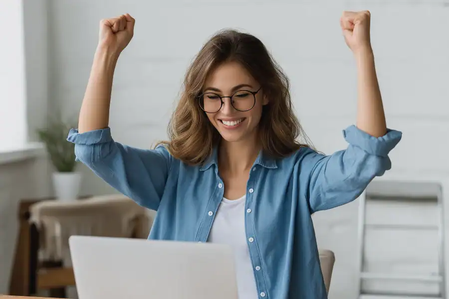 Happy woman celebrating success at work using a laptop, positive emotion, and achievement.