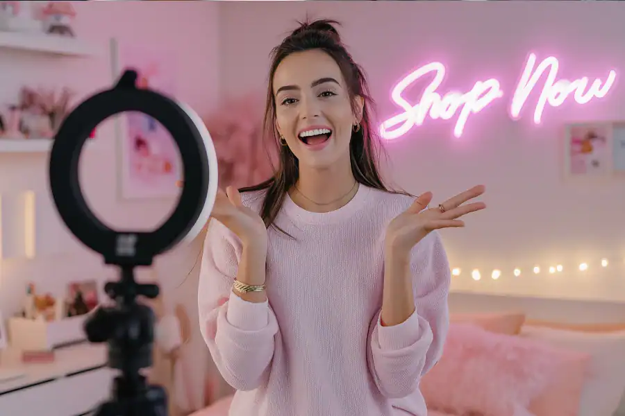 Bright young woman recording beauty or lifestyle content with ring light in stylish pink-themed room.