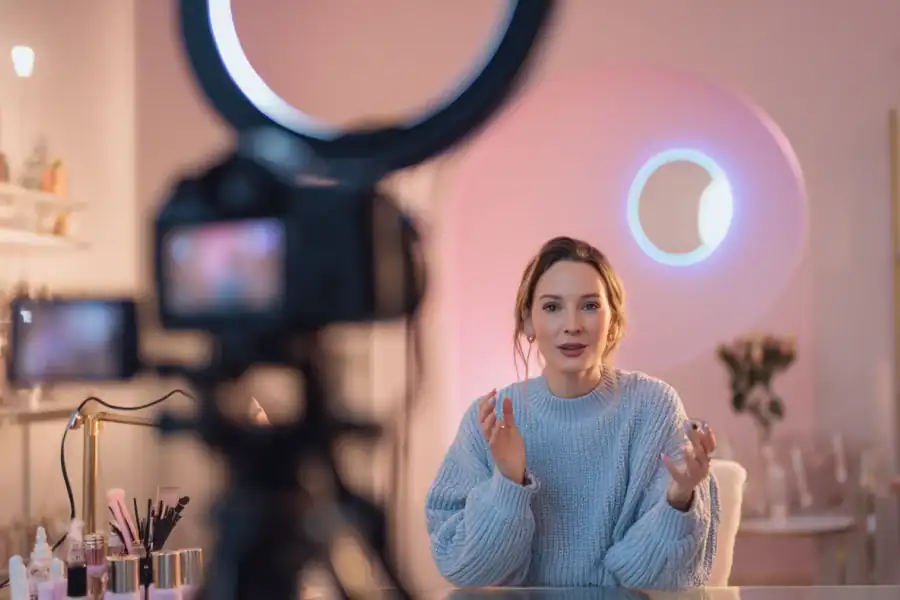 Bright beauty influencer recording makeup tutorial with professional camera setup in stylish pink room.